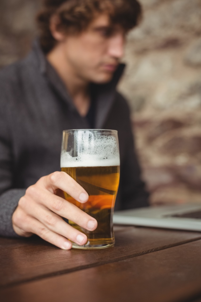 Homem no bar, segurando uma tulipa de cerveja na mesa de madeira